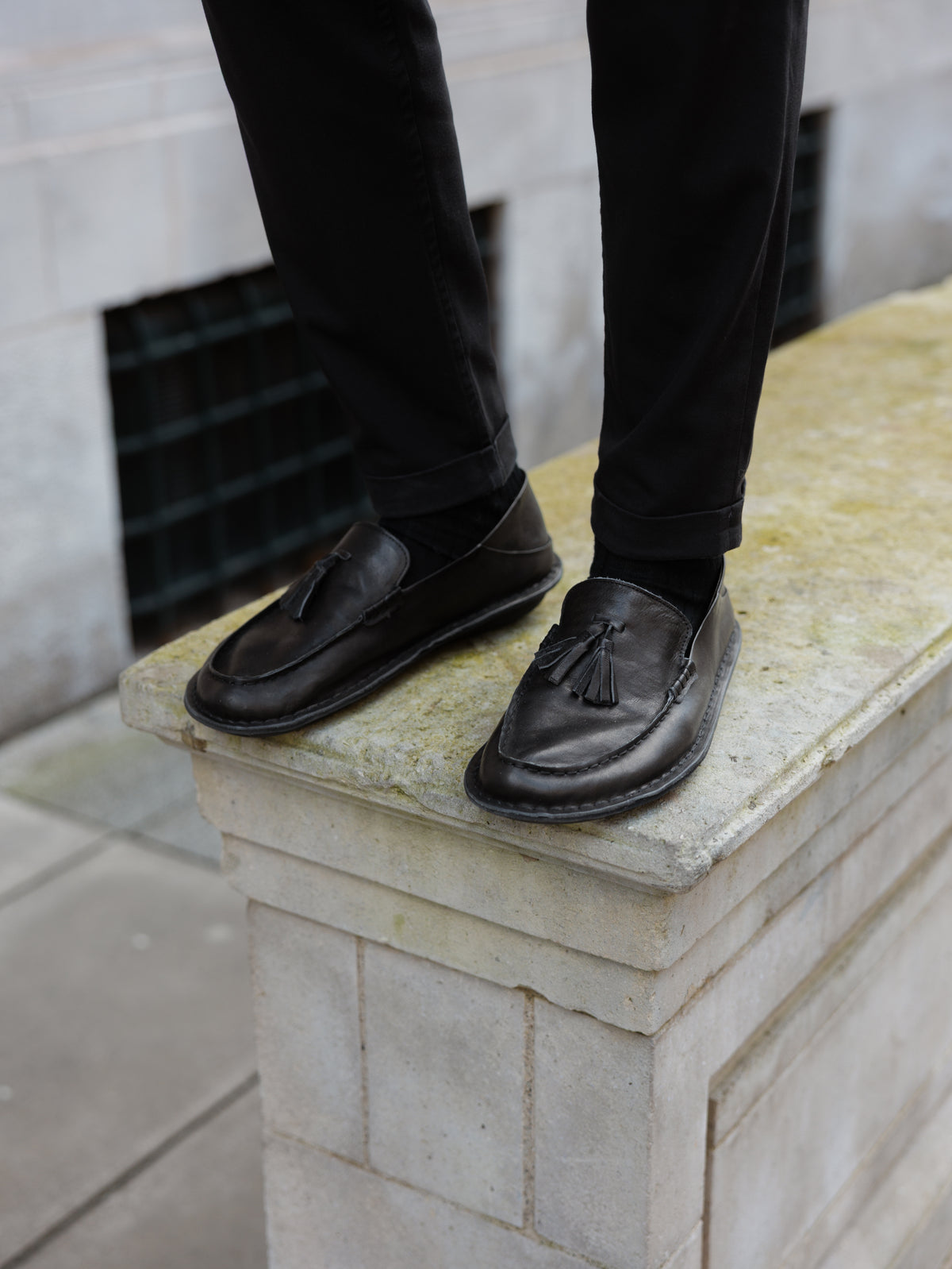 Persona de pie sobre un muro de piedra con mocasines TRIBECA negros