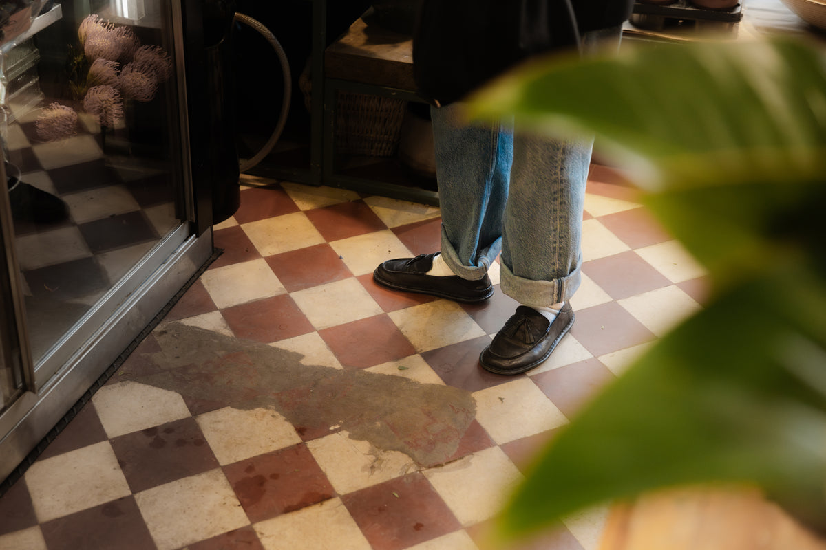 Mocasines TRIBECA negros y jeans sobre un piso de baldosas a cuadros