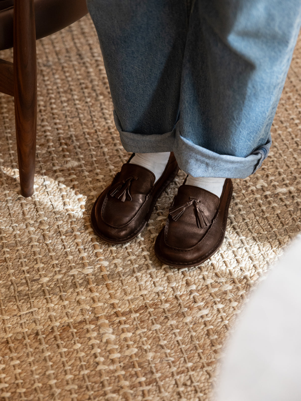 Mocasines TRIBECA Cocoa Brown con jeans y calcetines blancos sobre una alfombra de yute