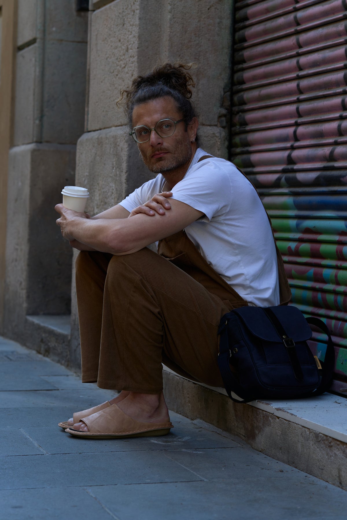 Hombre sentado en la vereda con un café, usando sandalias SAINT TROPEZ de cuero claro
